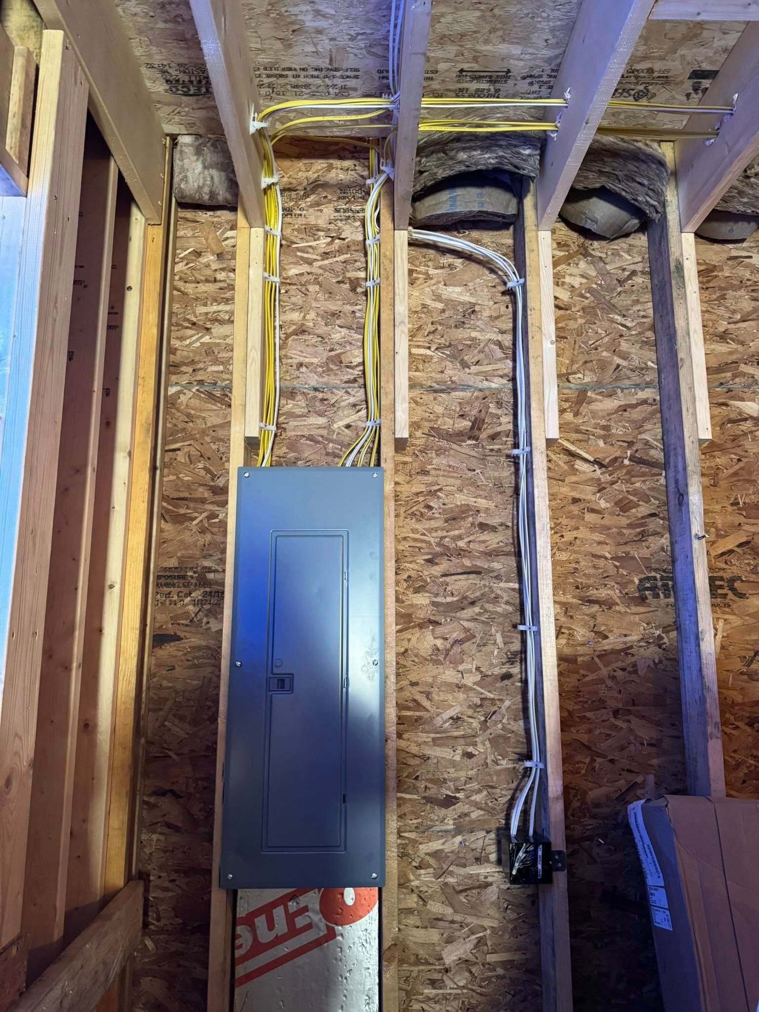 Electrical panel installed between wooden studs, with wiring visible.