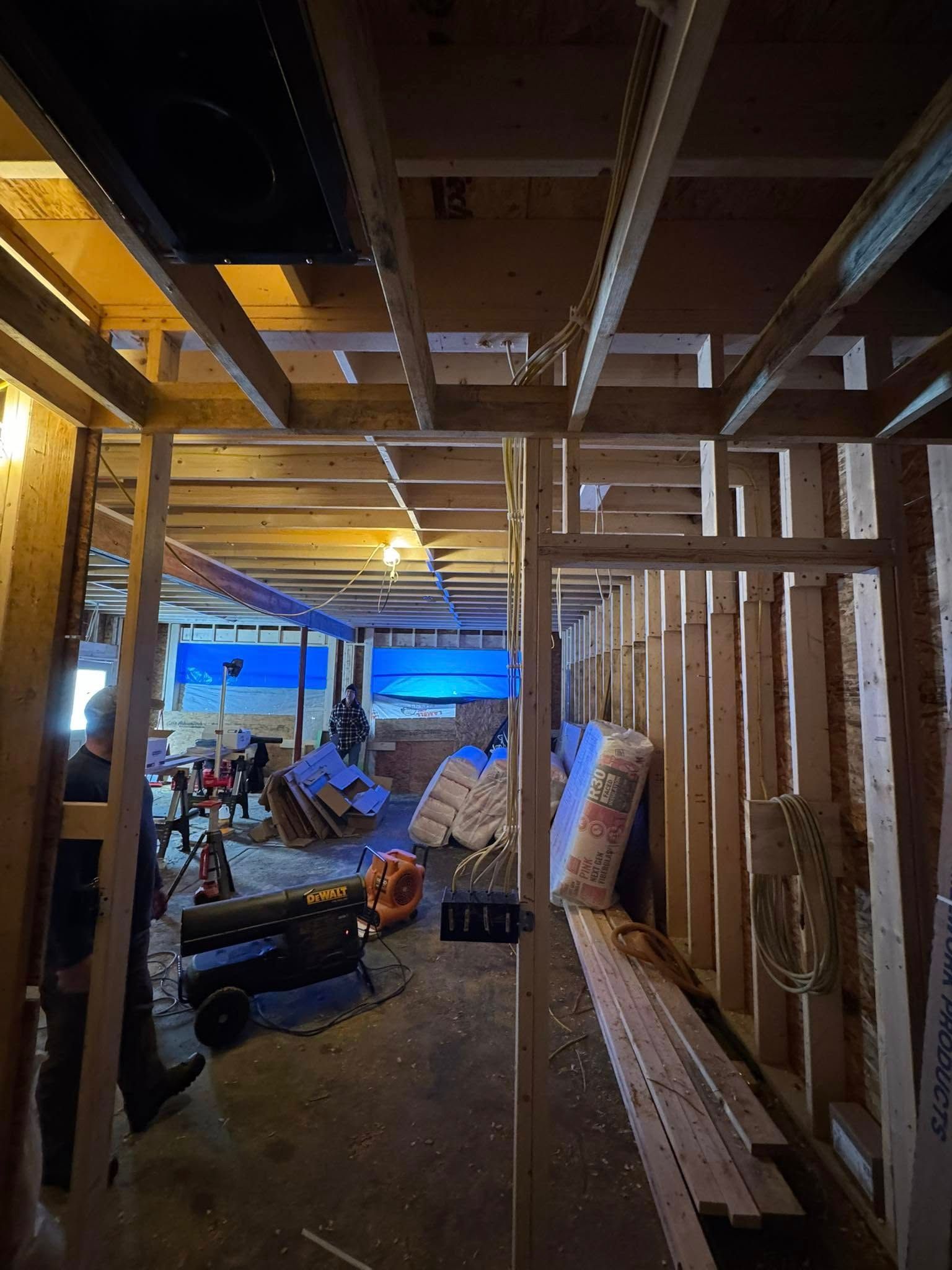 Basement under construction, wooden framing, tools, insulation, and a person visible.