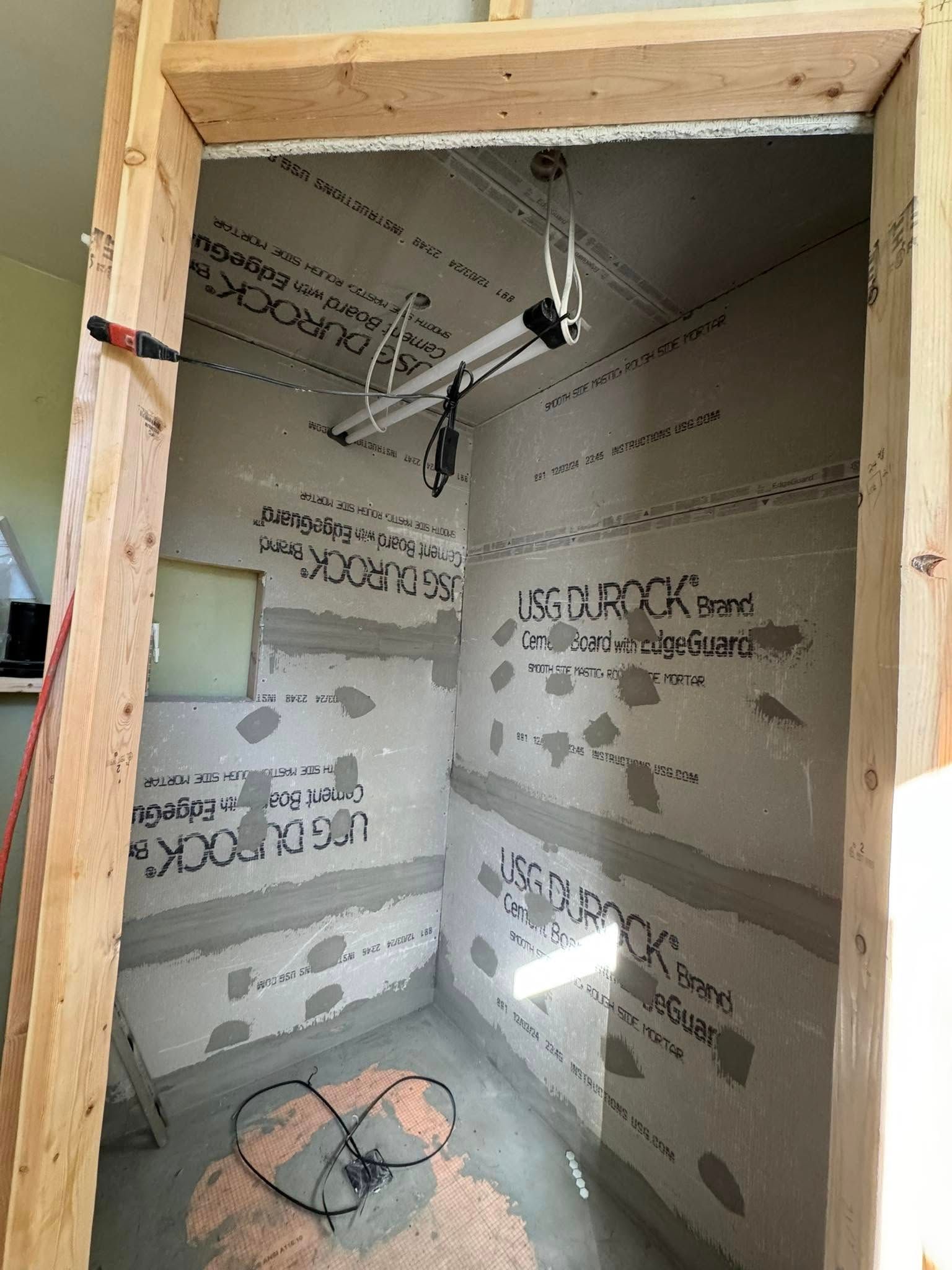 Shower stall under construction, gray walls with applied waterproofing, unfinished wooden frame.