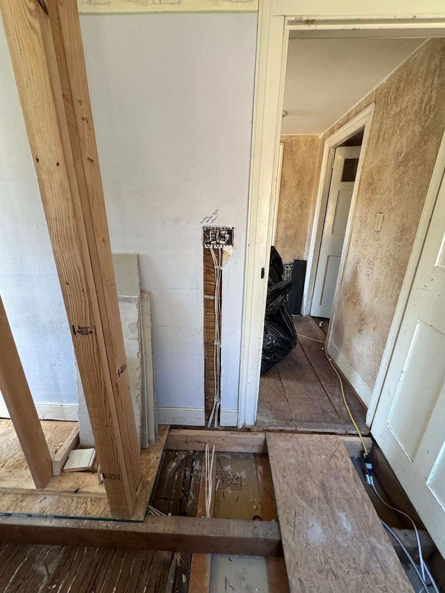 Hallway under renovation; exposed wooden framing, missing flooring, open doorways, debris.