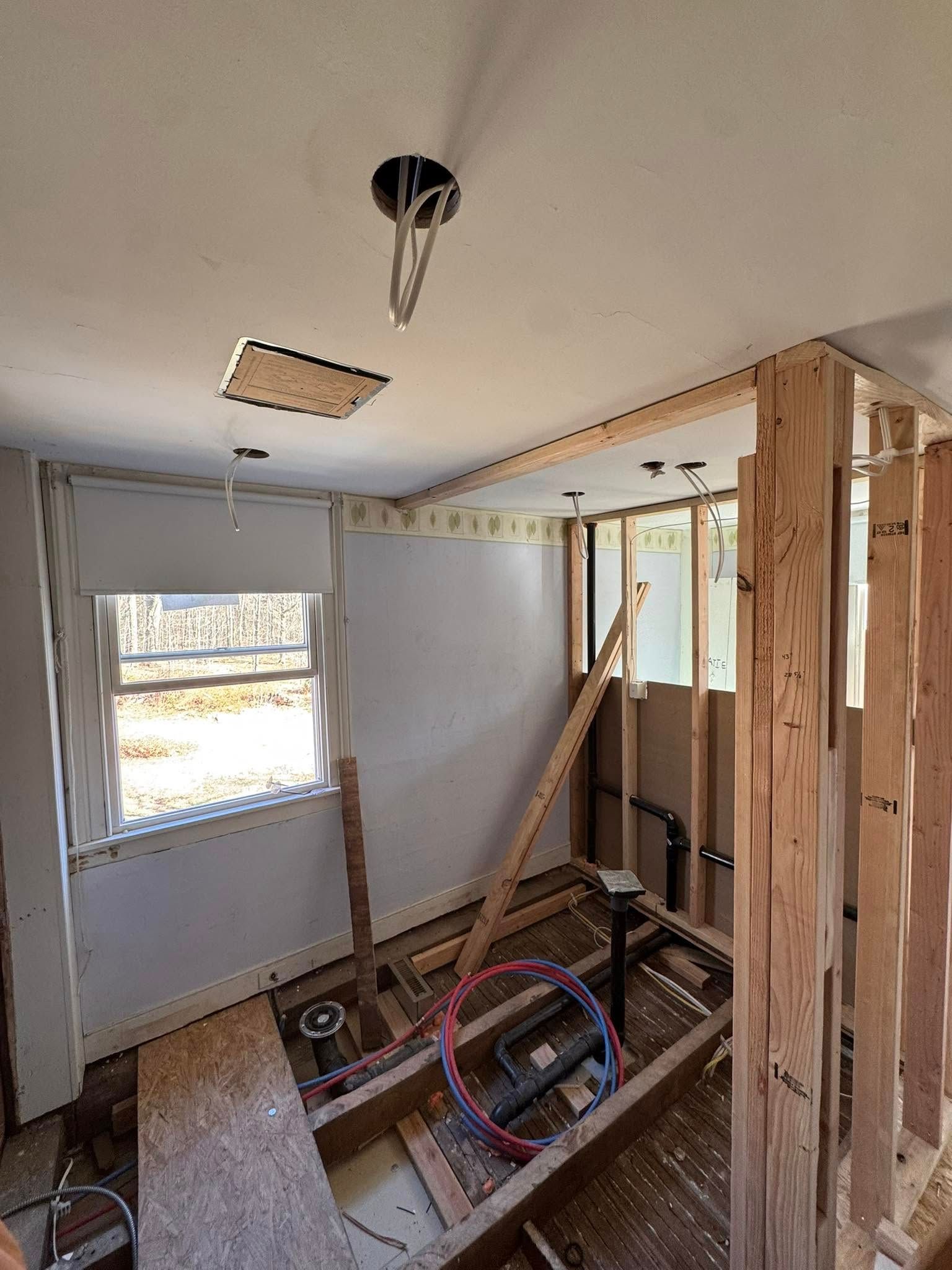 Bathroom under construction, showing framing, window, plumbing, and exposed ceiling wiring.