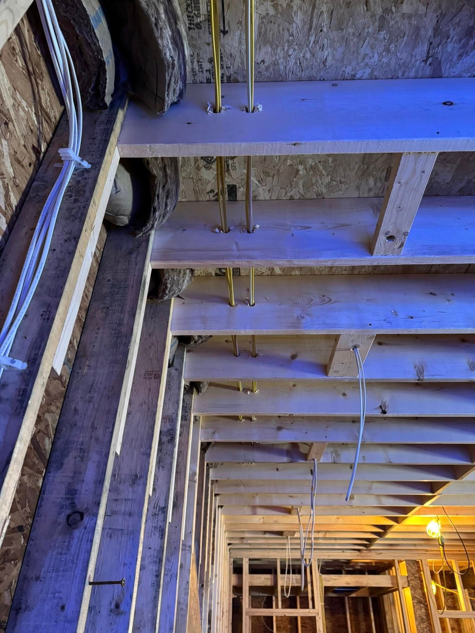 Construction of a ceiling with exposed wooden beams, electrical wiring, and plumbing.