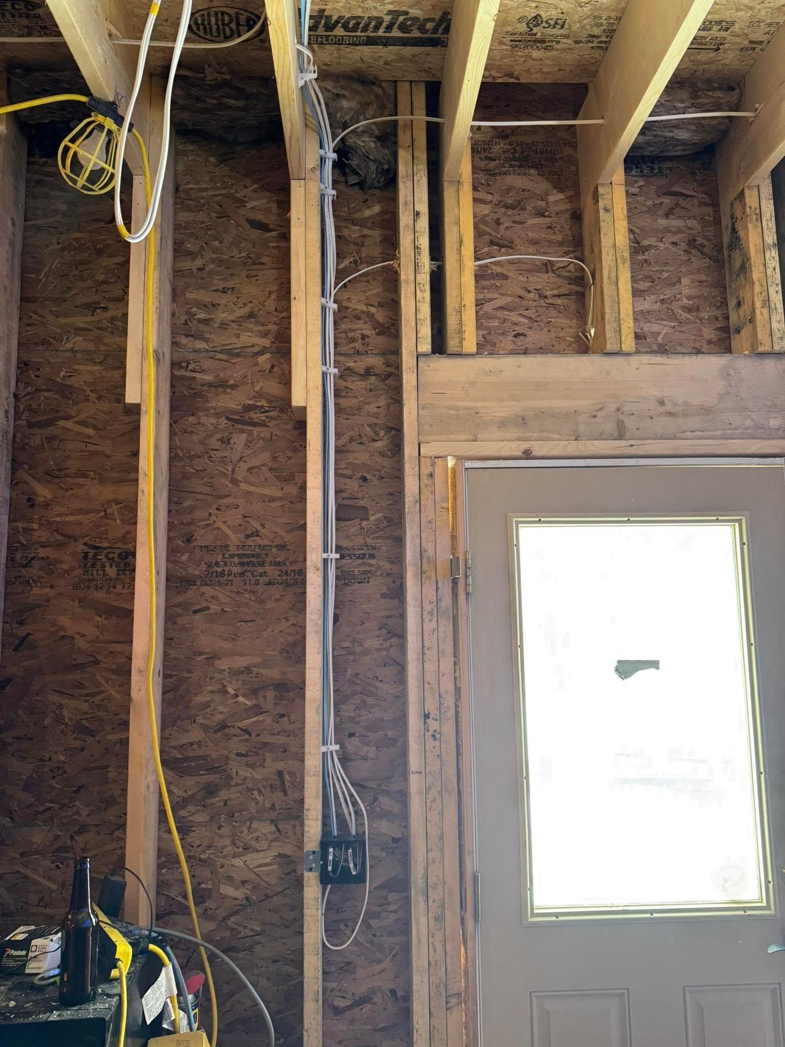 Electrical wiring in a wall under construction, with a door and plywood sheathing.