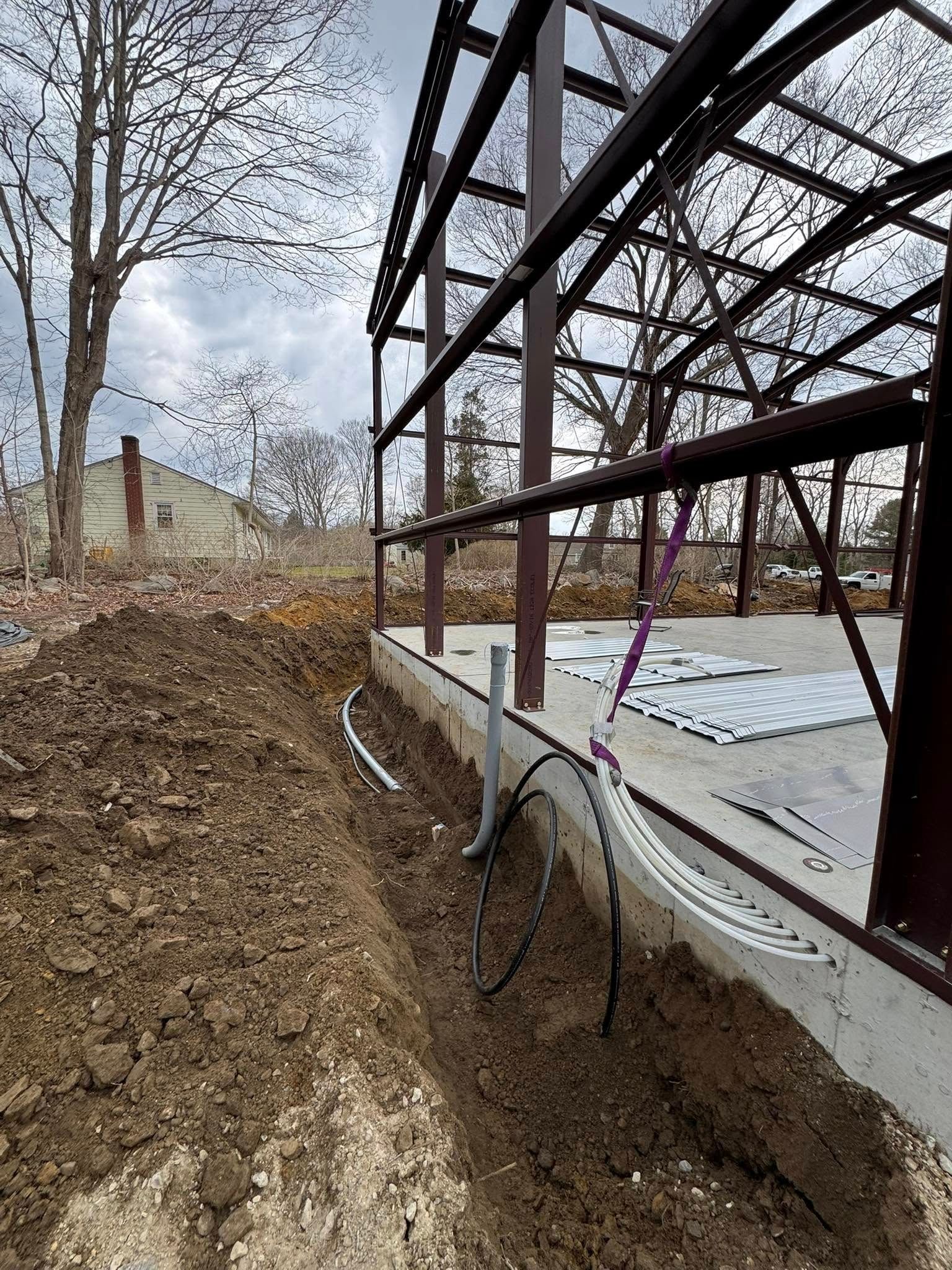 Construction site with steel frame structure, exposed electrical wiring in trench next to concrete foundation.