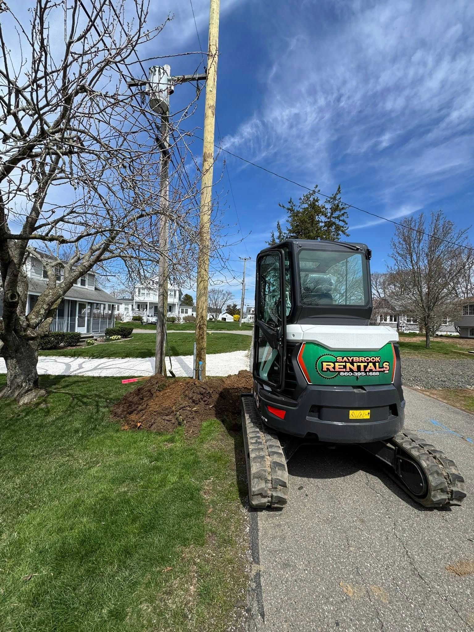 Mini excavator next to a utility pole on a sunny day; residential setting.