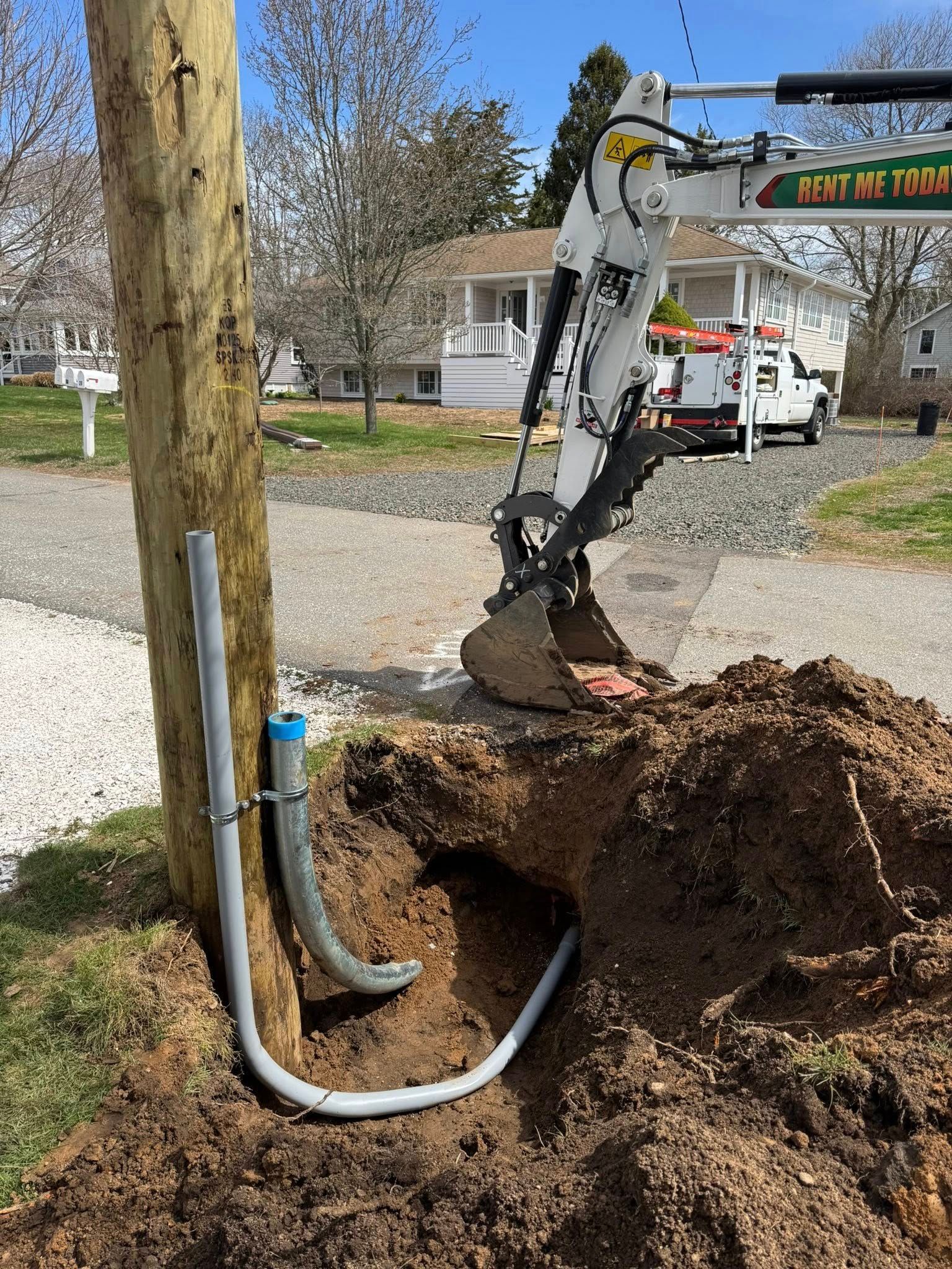 An excavator digging near a utility pole, exposing buried conduit. A utility truck is parked nearby.