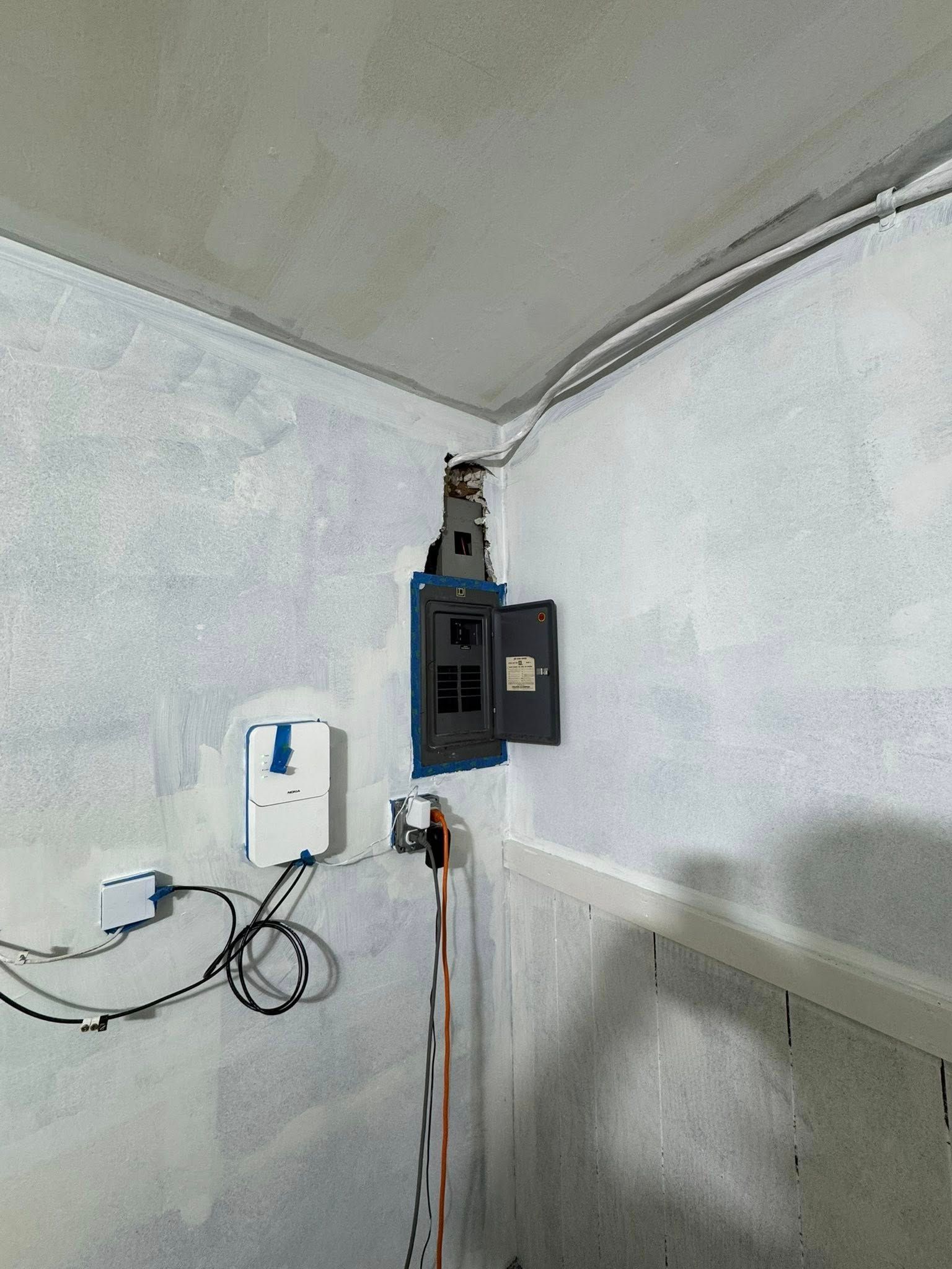 Electrical panel and related devices mounted on a light blue-painted corner wall.