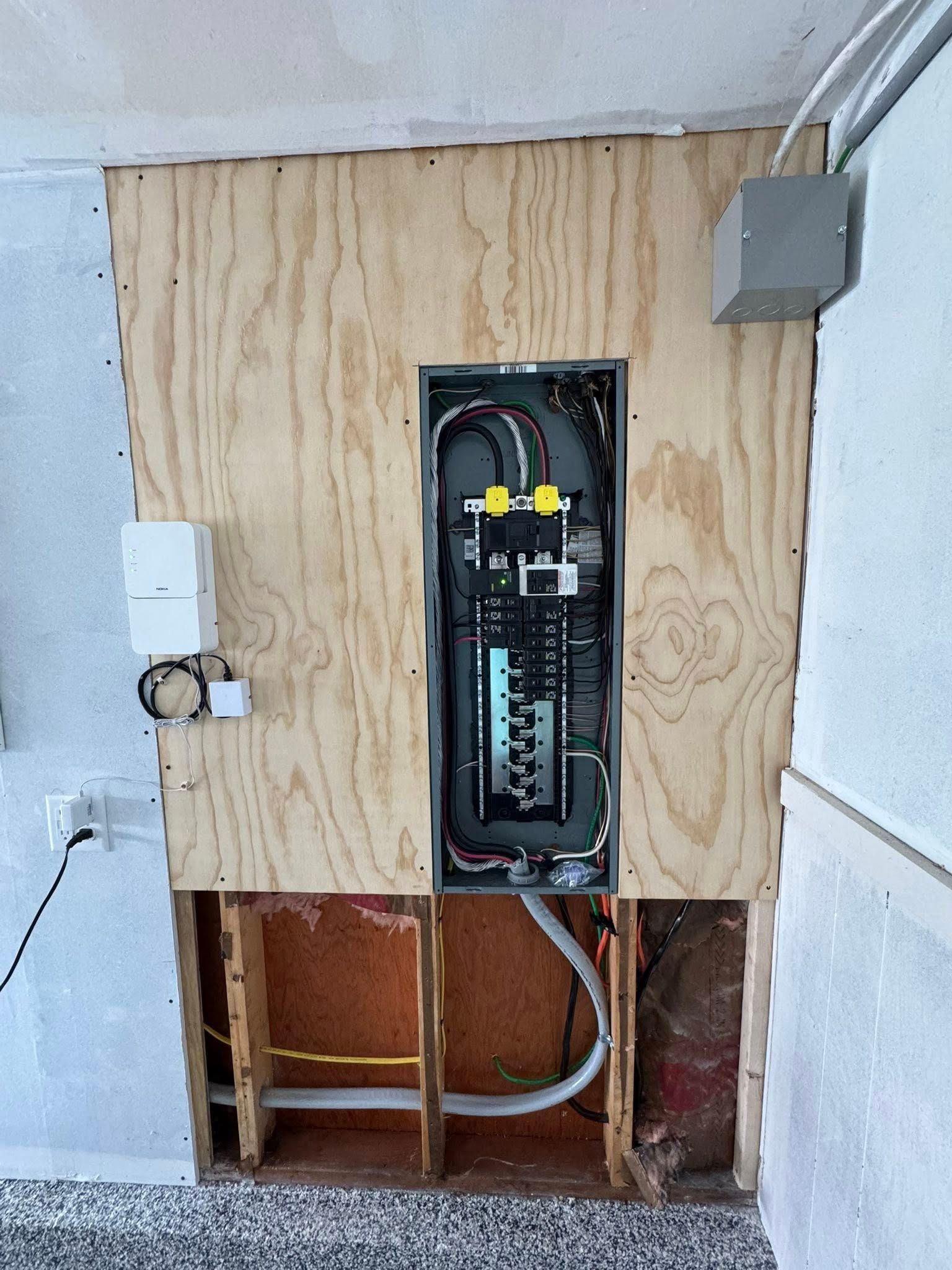 Electrical panel installation in a wall; plywood backing, conduits, and wire management.