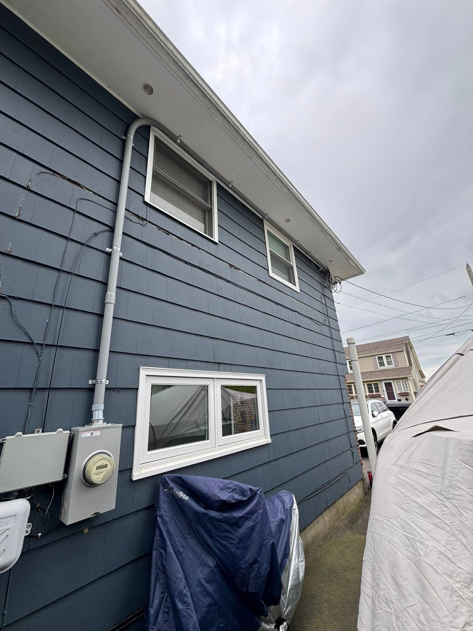 Dark blue siding on a house with windows, electrical conduit, and a covered object on the right.