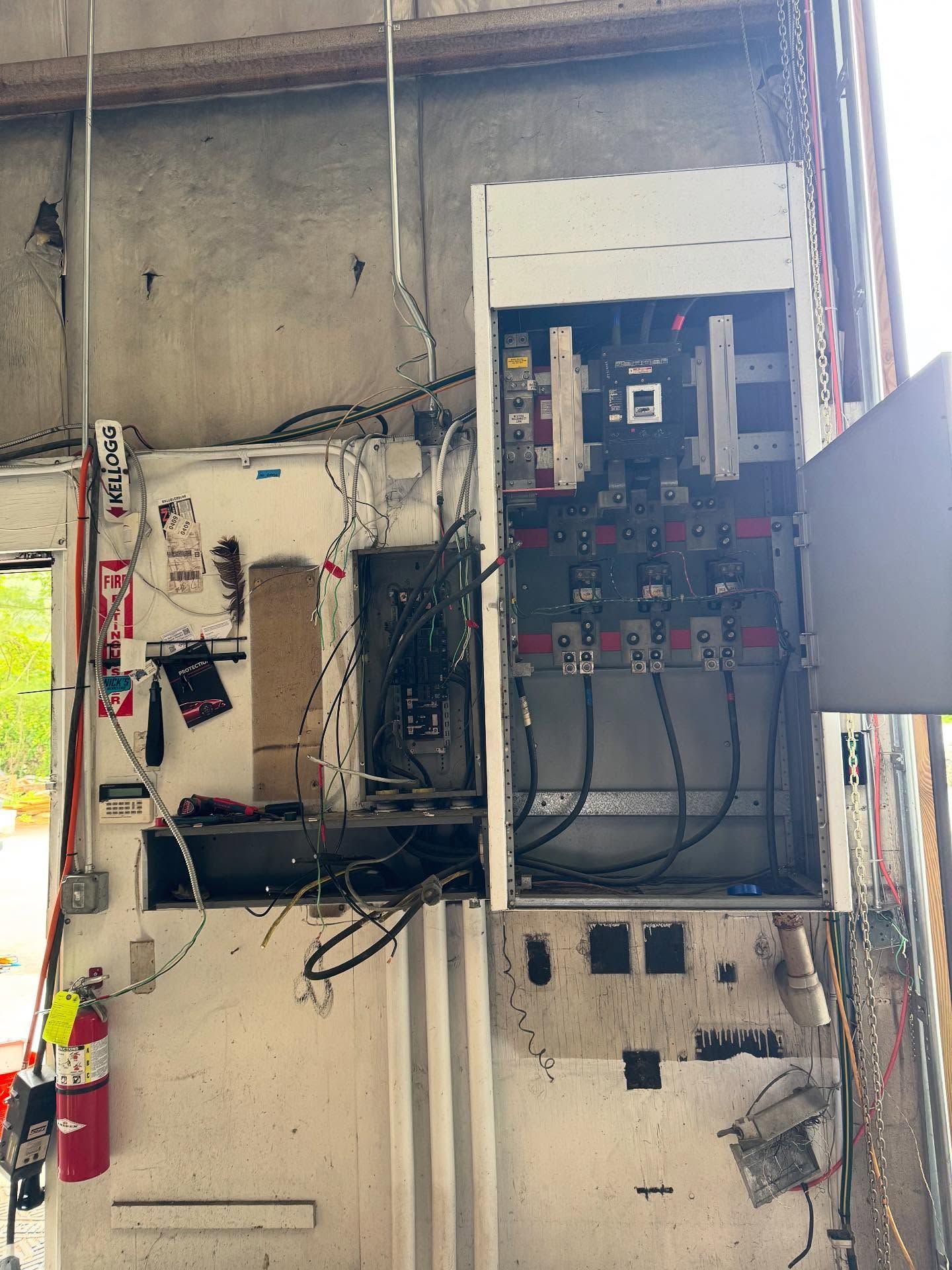 Open electrical panel on a wall with exposed wiring and a fire extinguisher.