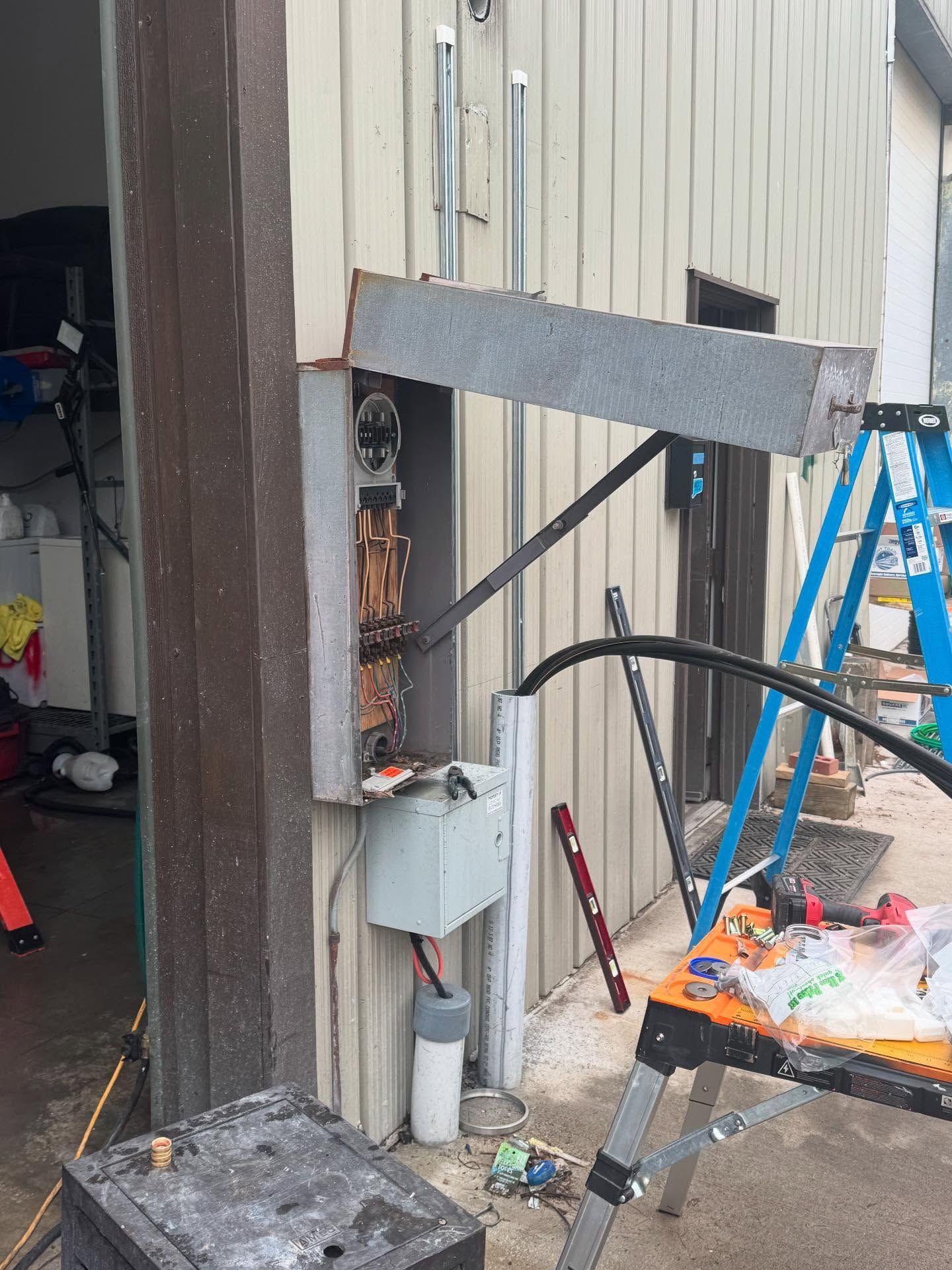 Electrical panel mounted on a building's exterior with conduit and wiring visible; construction tools nearby.