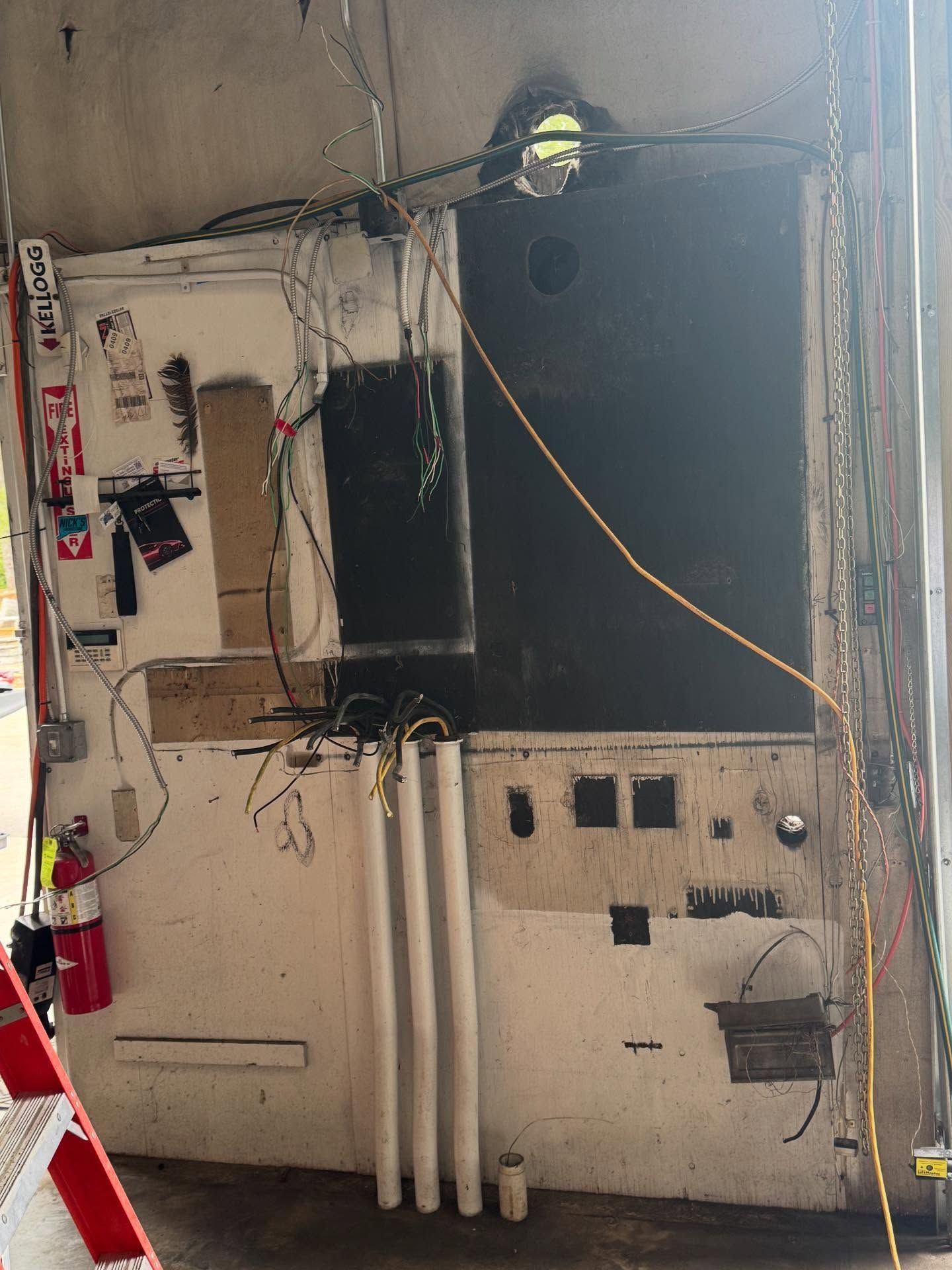 Messy electrical panel with exposed wires, fluorescent lights, and a fire extinguisher.