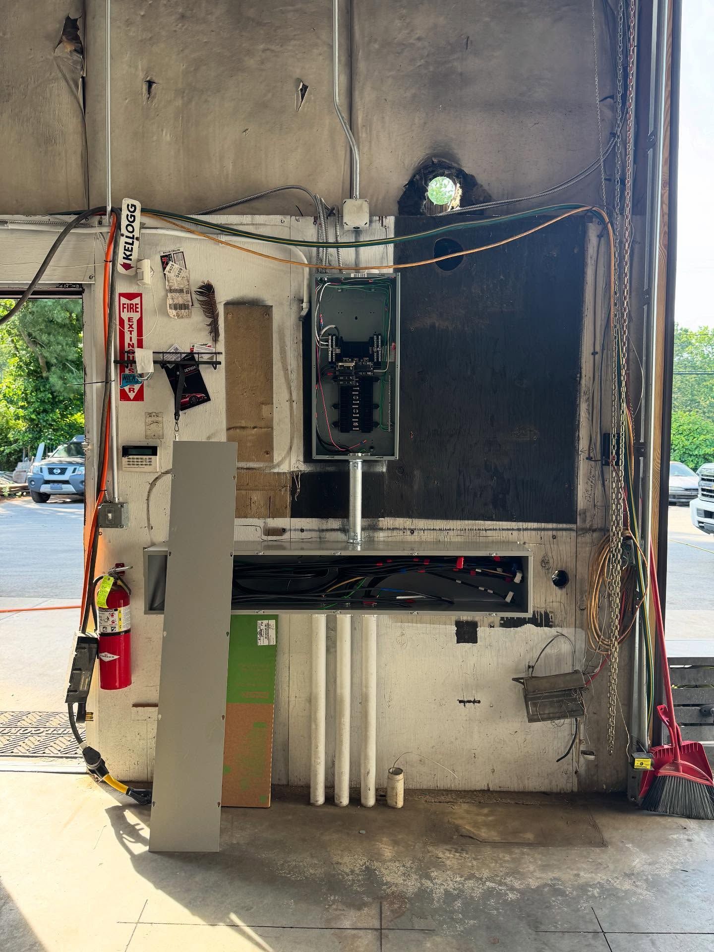 Large industrial machine with electrical components, fire extinguisher, and wiring. Located in a garage or workshop setting.