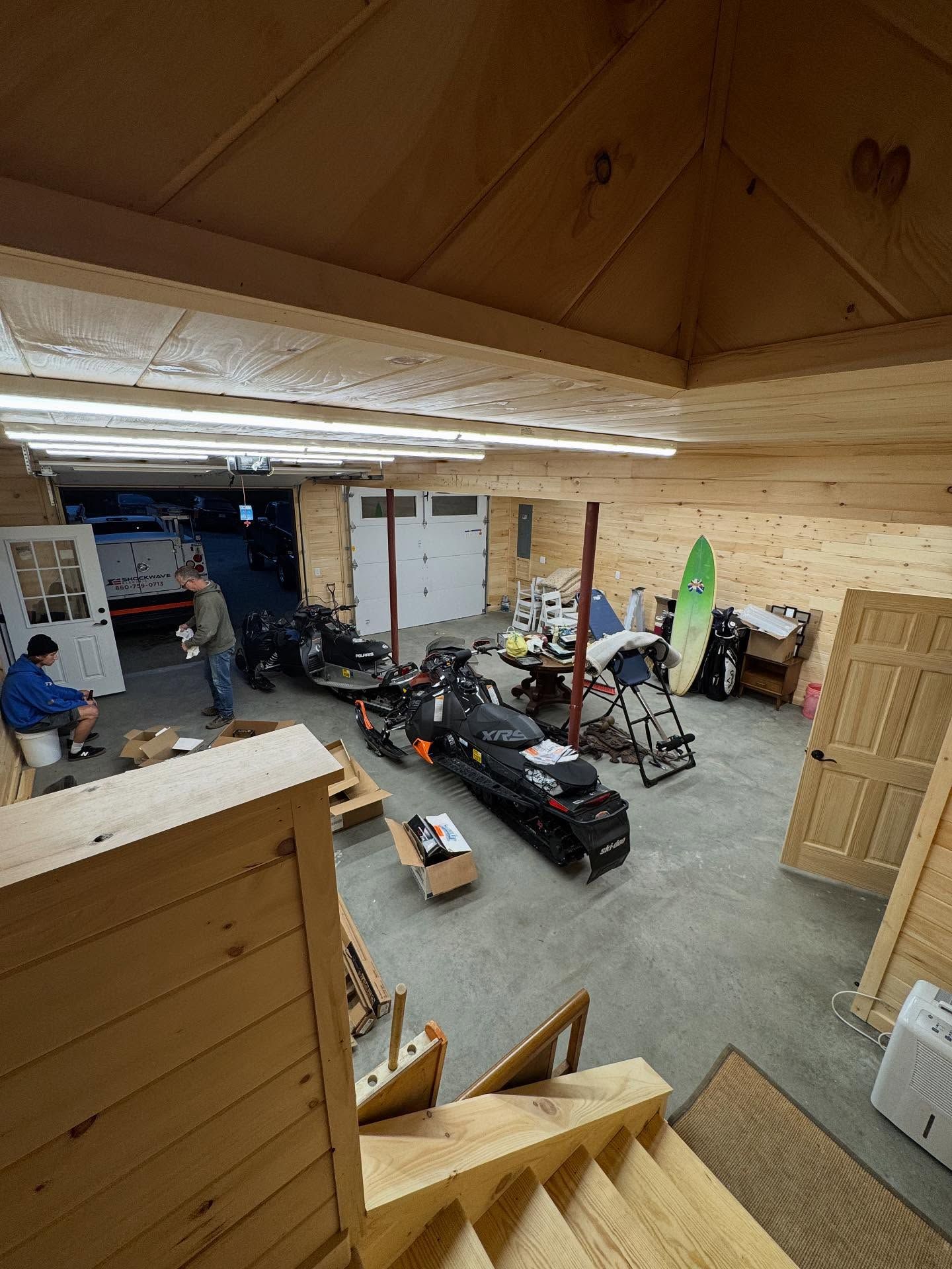 Wooden garage with snowmobiles, people, and doors.