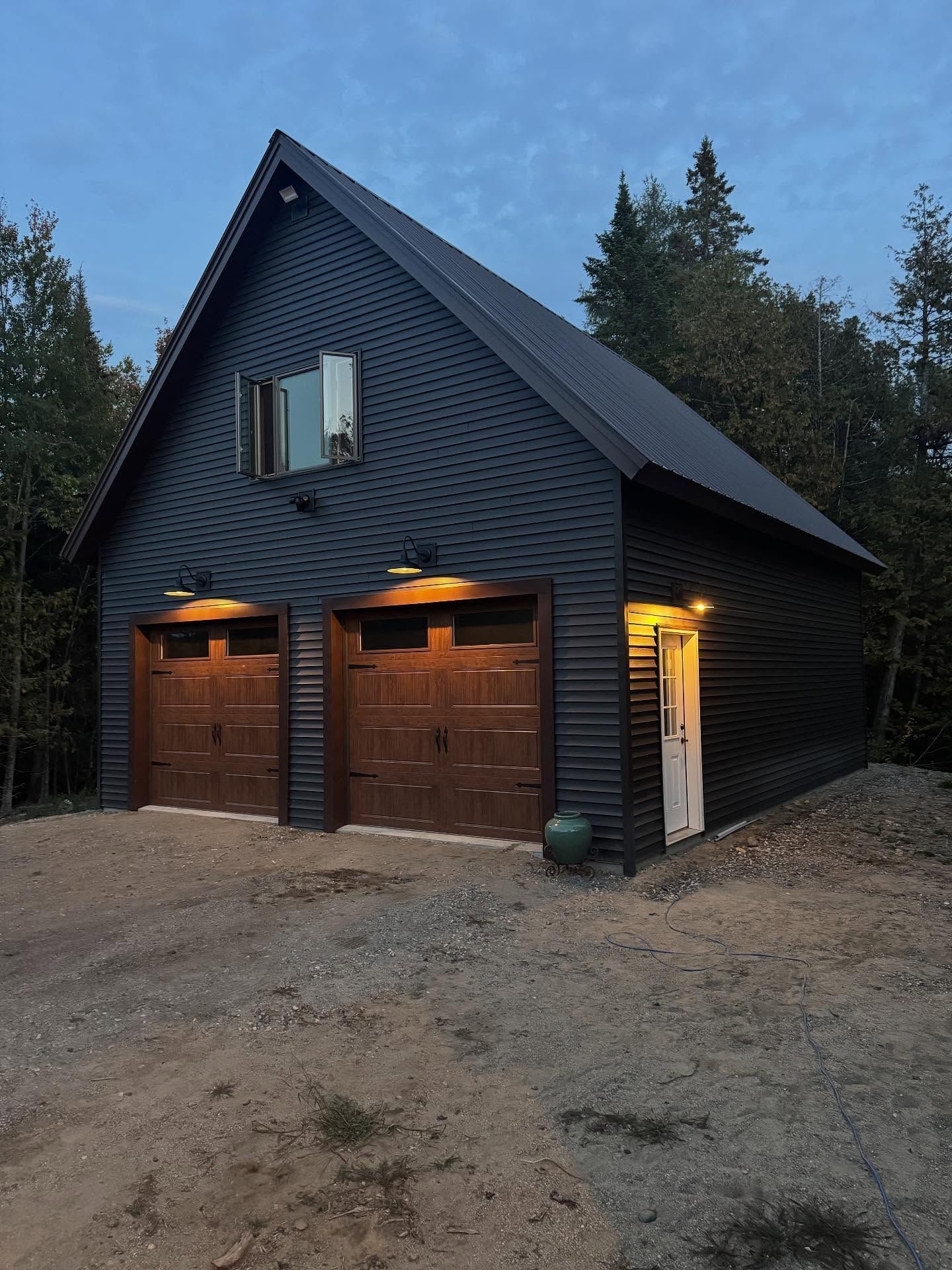 Black two-story garage with brown garage doors, white side door, and single window. Lit by exterior lights.