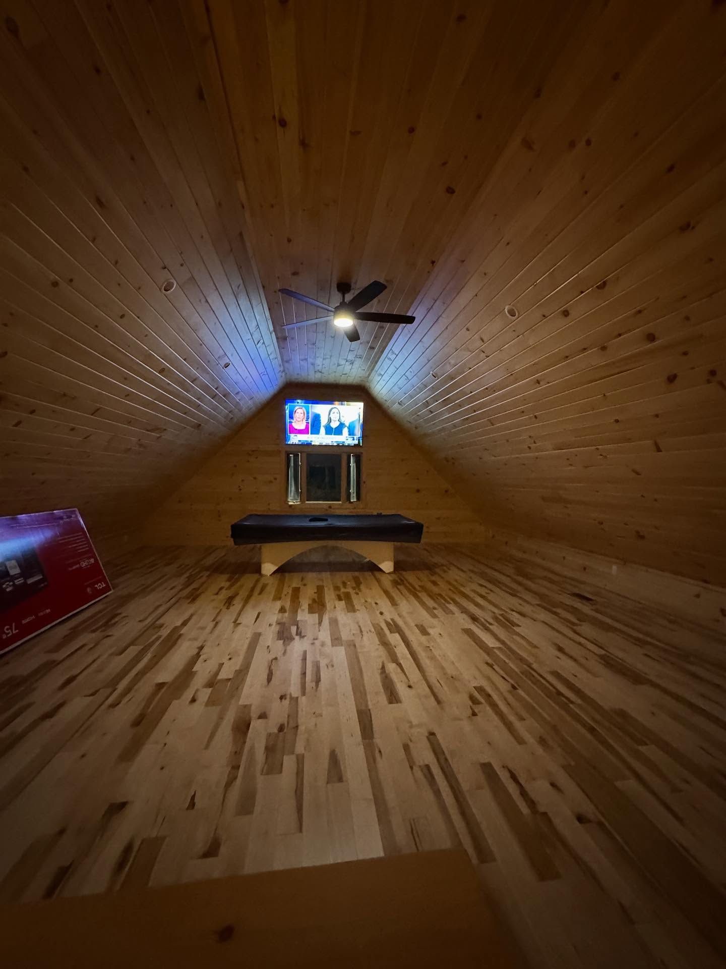 Wooden attic room with a TV, a bench, and a ceiling fan.