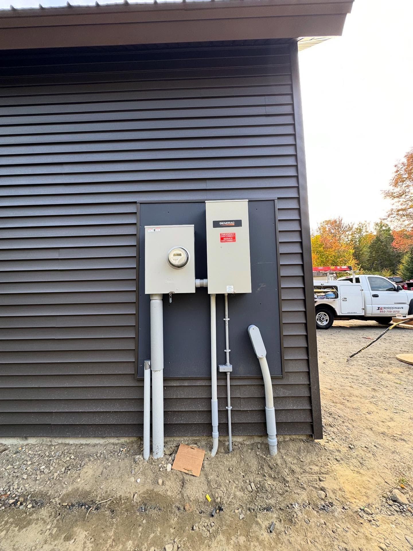 Exterior electrical panel on a dark brown building with conduit and a utility truck in the background.