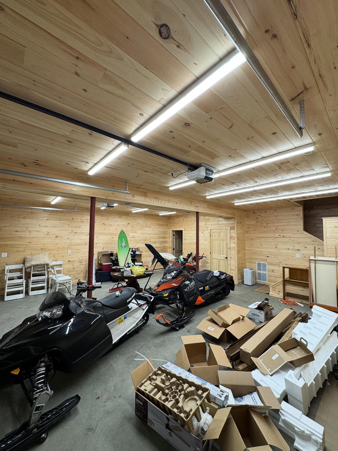 Garage interior with snowmobiles, boxes, shelving, and wooden walls.