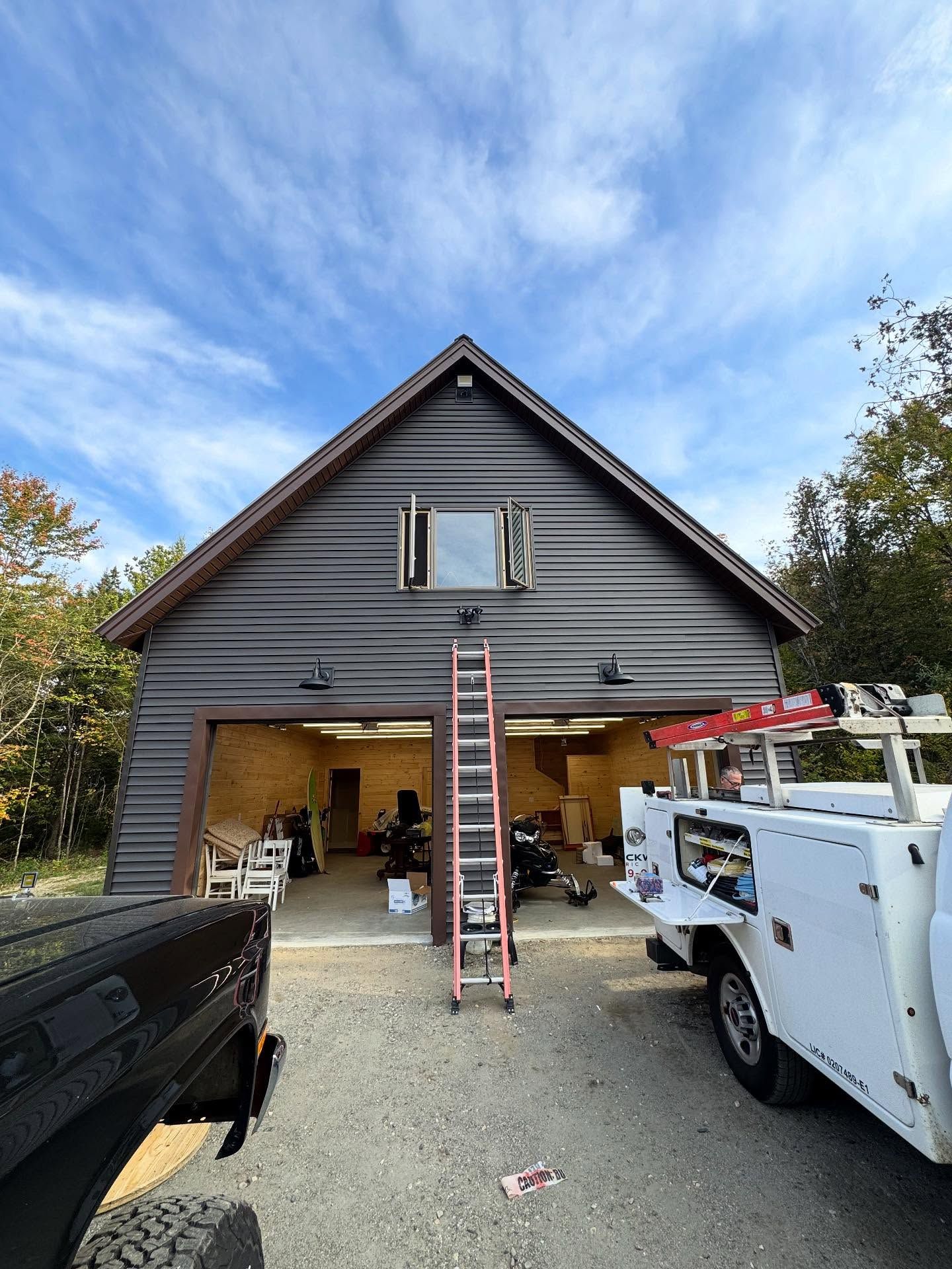 Garage with open door, wooden siding, ladder in front, white service truck, blue sky.