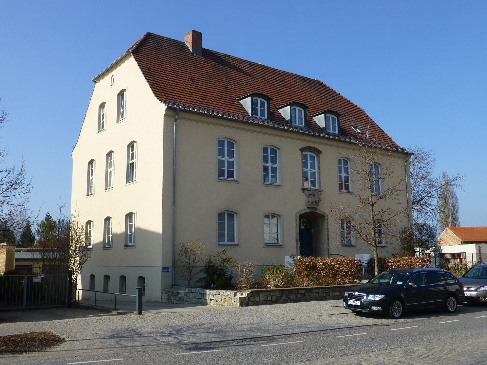 A large white building with a brown roof and a black suv parked in front of it