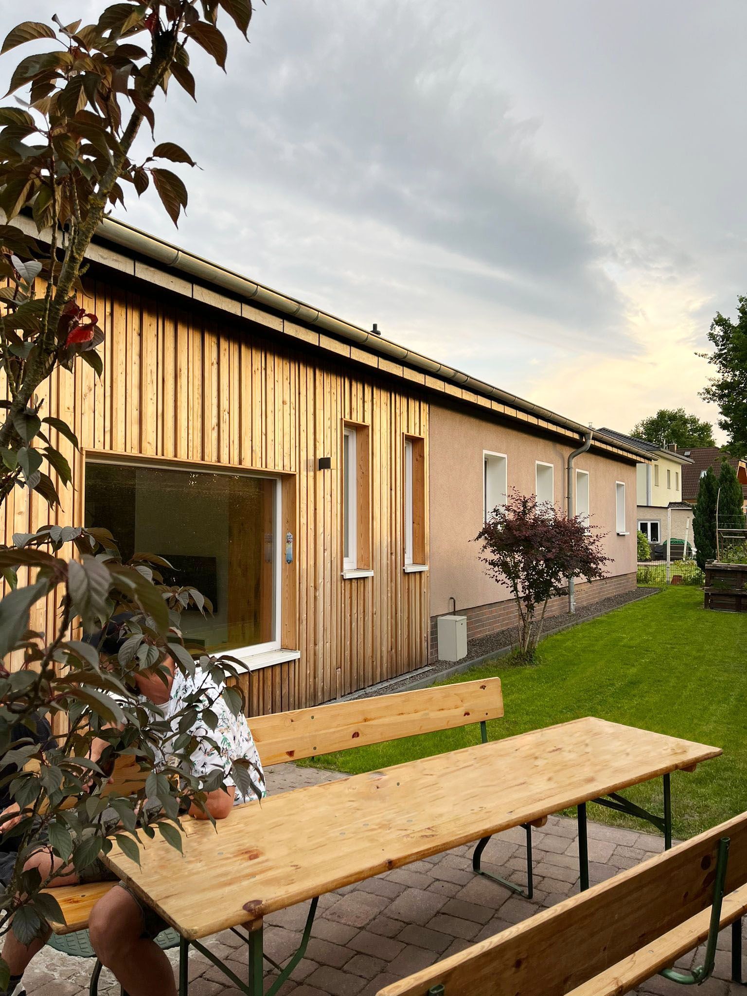 A man sits at a wooden table in front of a house