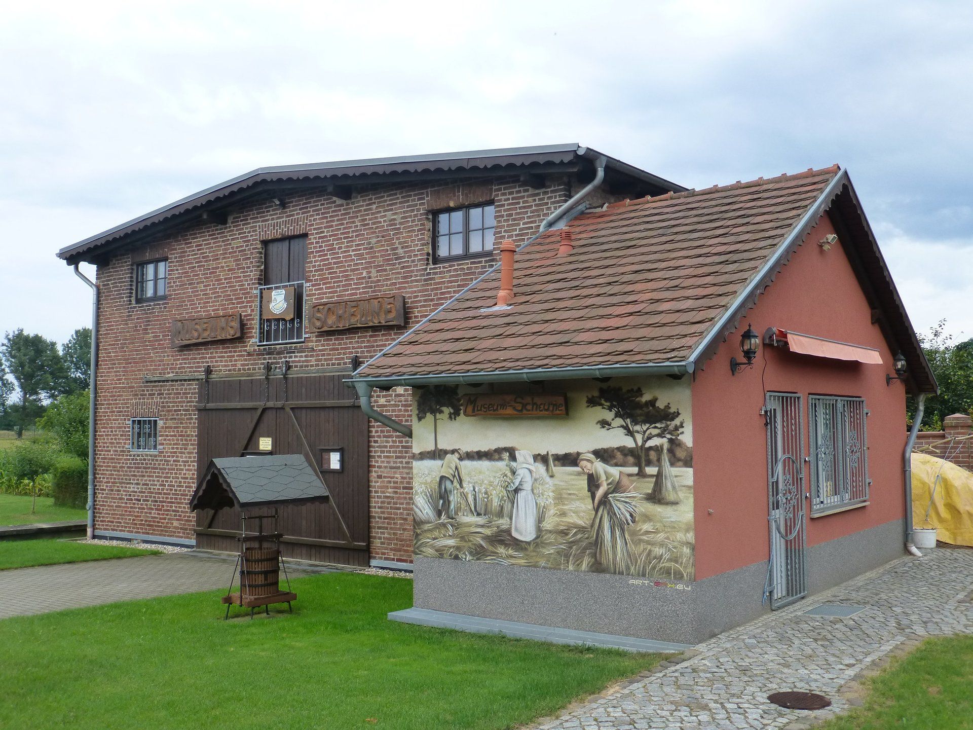 A brick building with a red roof and a well in front of it