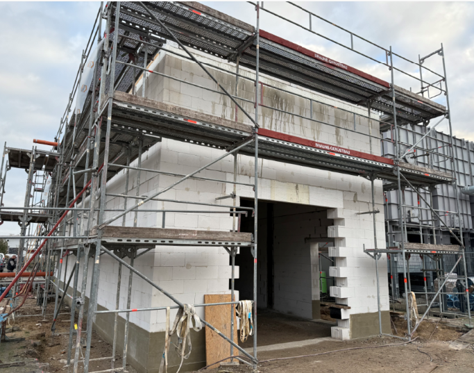 Eingebautes Gebäude mit Gerüst. Weiße Ziegelwände, offene Tür, graues Gerüst ringsum.