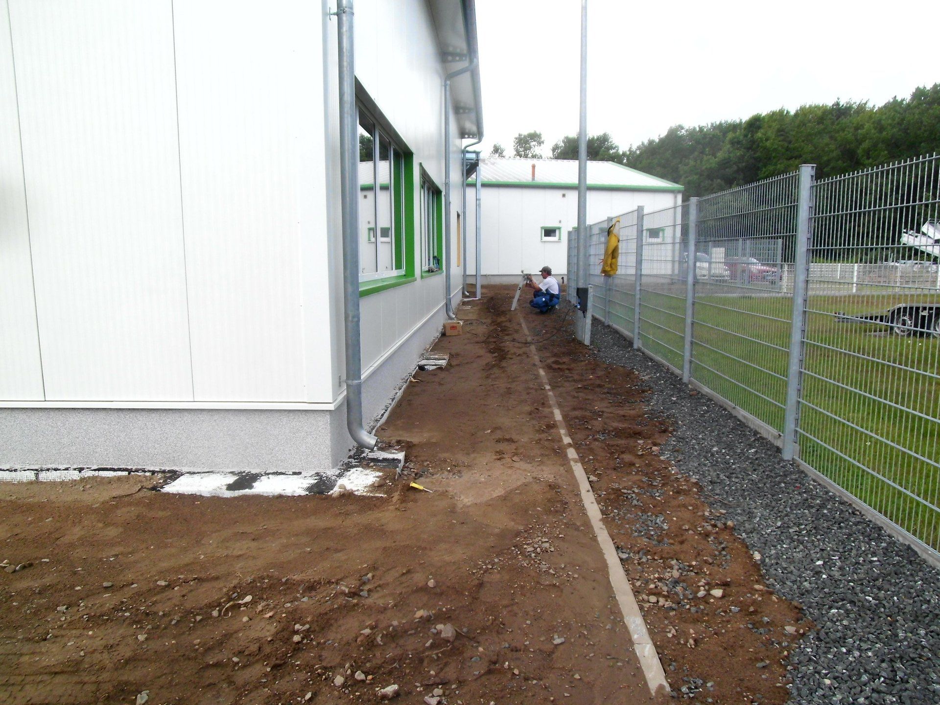 A man sits on the side of a building next to a fence