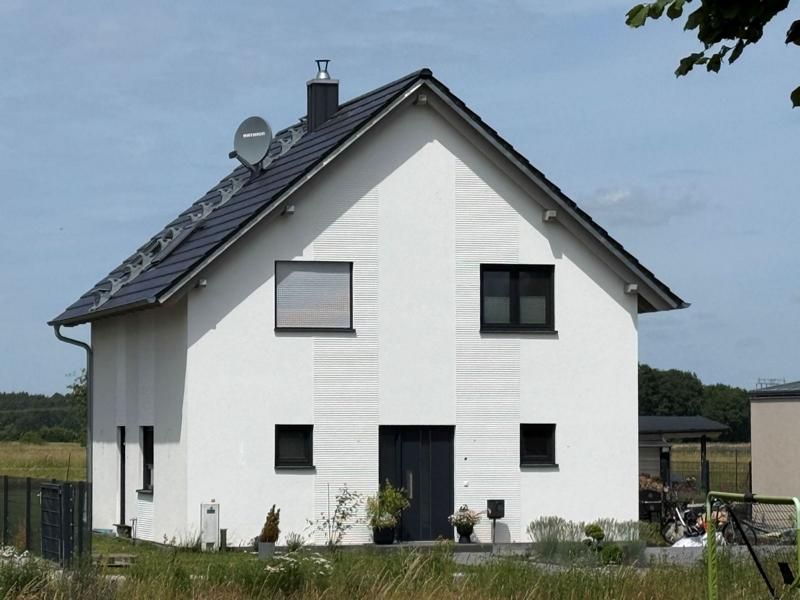 Weißes zweistöckiges Haus mit dunklem Dach und kleinen Fenstern an der Vorderseite in ländlicher Feldlage