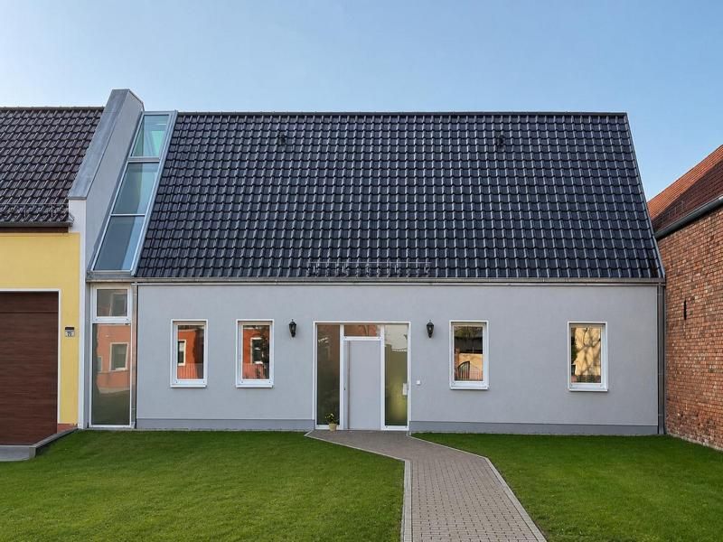 Graues Haus mit schwarzem Dach und Glasabschnitt, unfertiger Bau, bewölkter Himmel.