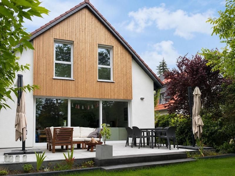 Modernes Haus mit holzverkleideter oberer Fassade, Terrassenmöbeln und Sonnenschirm in einem angelegten Garten