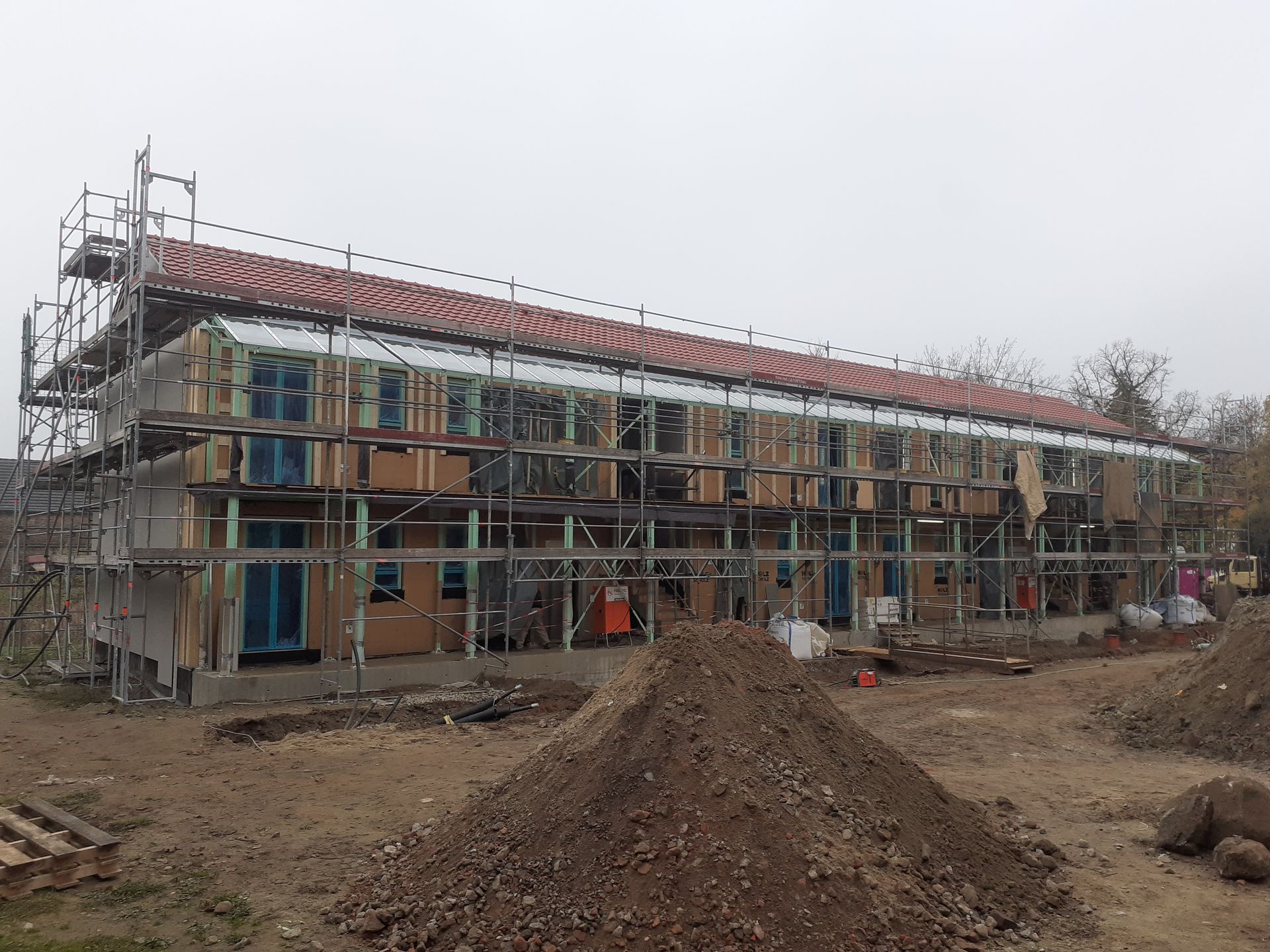 Ein im Bau befindliches Gebäude mit einem Gerüst und einem Erdhaufen davor.