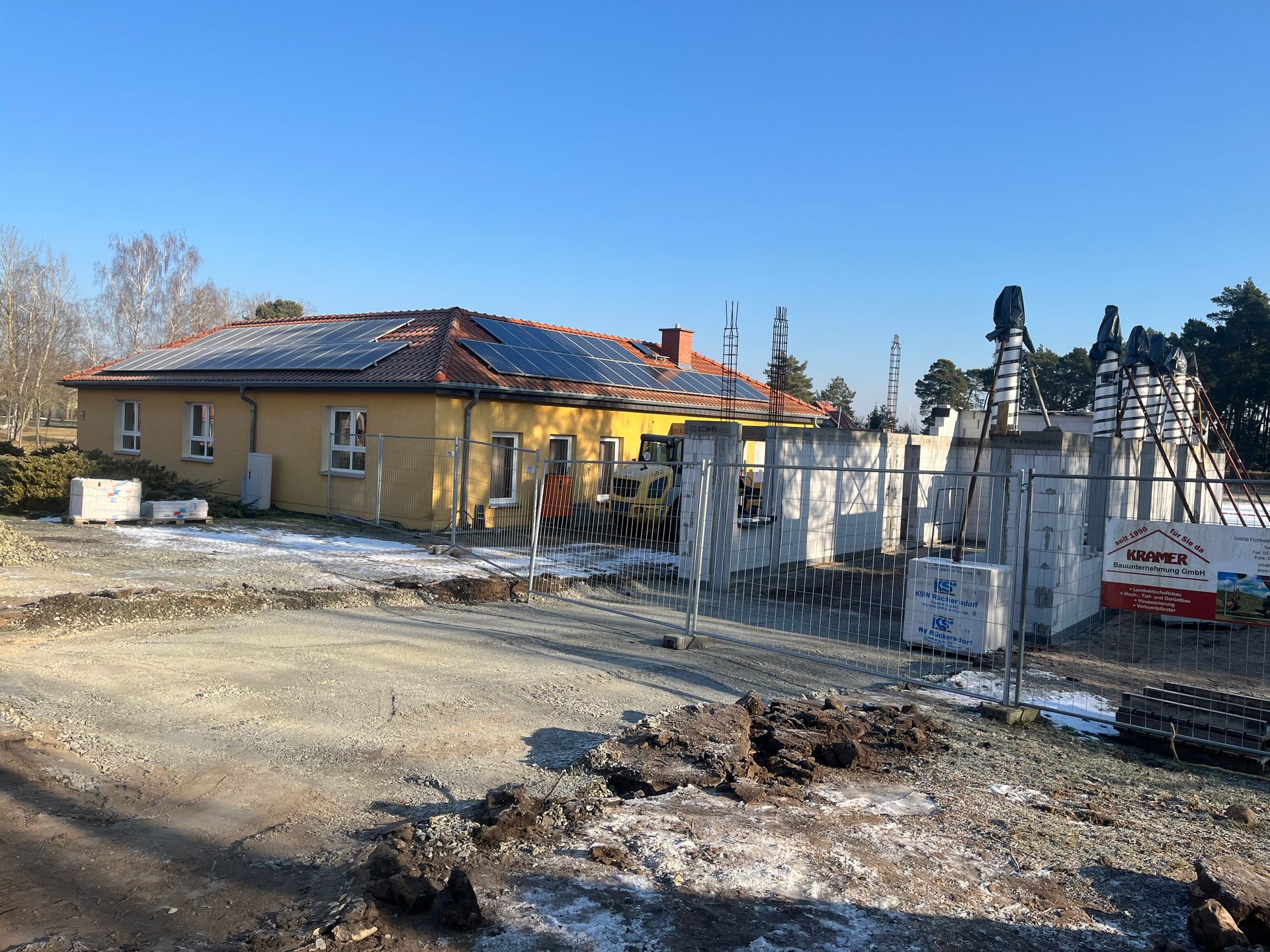 Baustelle mit einem gelben Gebäude, klarem Himmel und Bauzäunen.