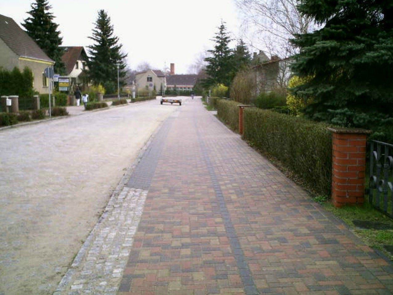 A brick walkway along a street with houses in the background