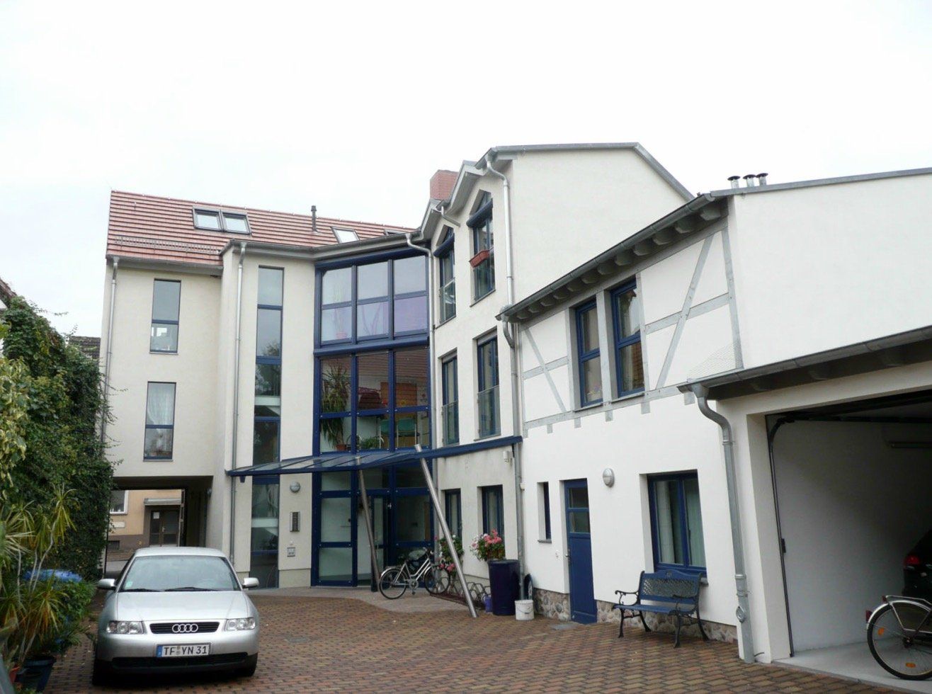 A silver car is parked in front of a large white building