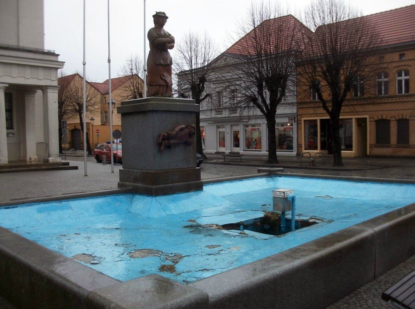 A fountain in a city with a statue in the background