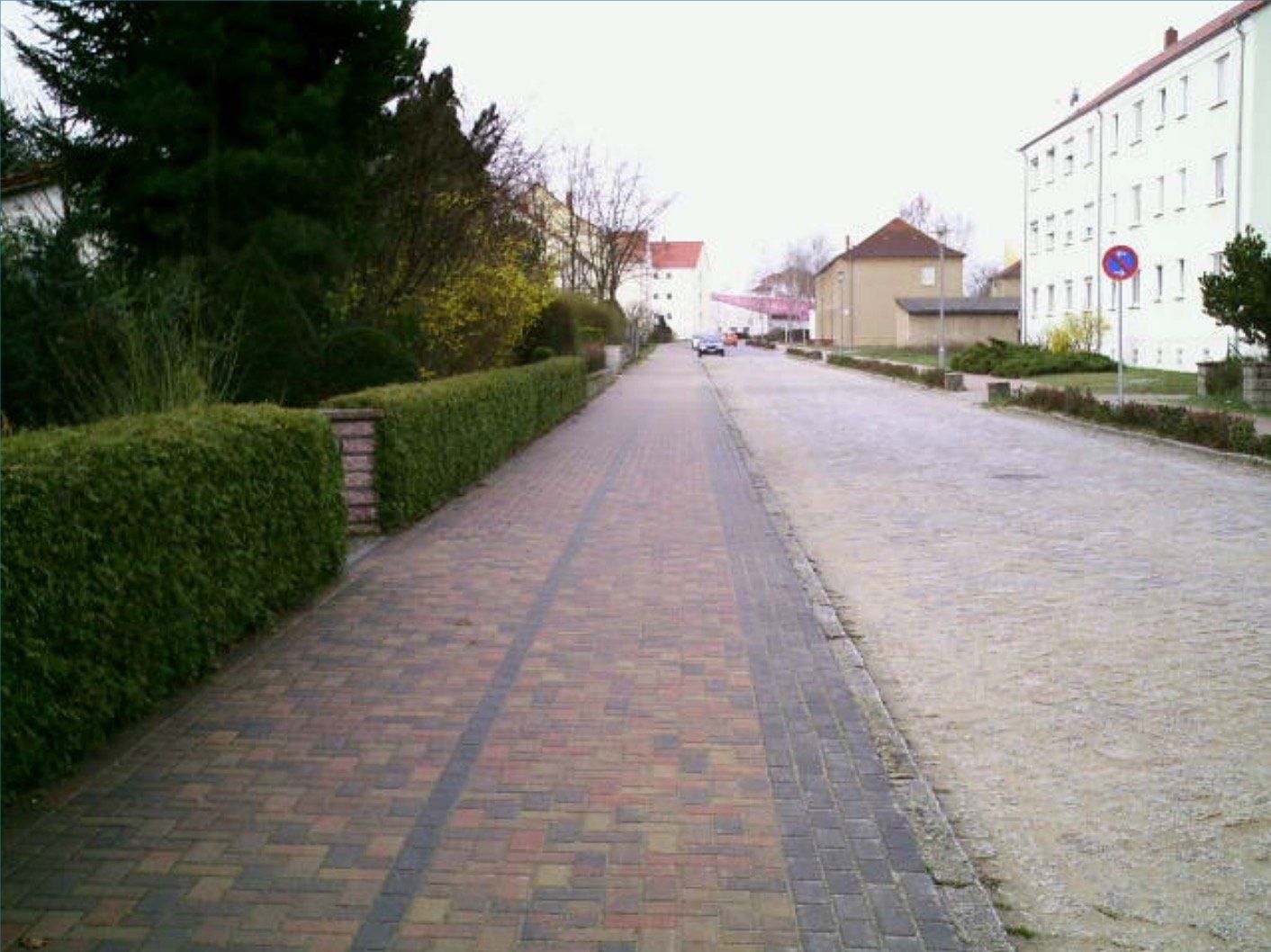 A brick walkway with a hedge on the side of it