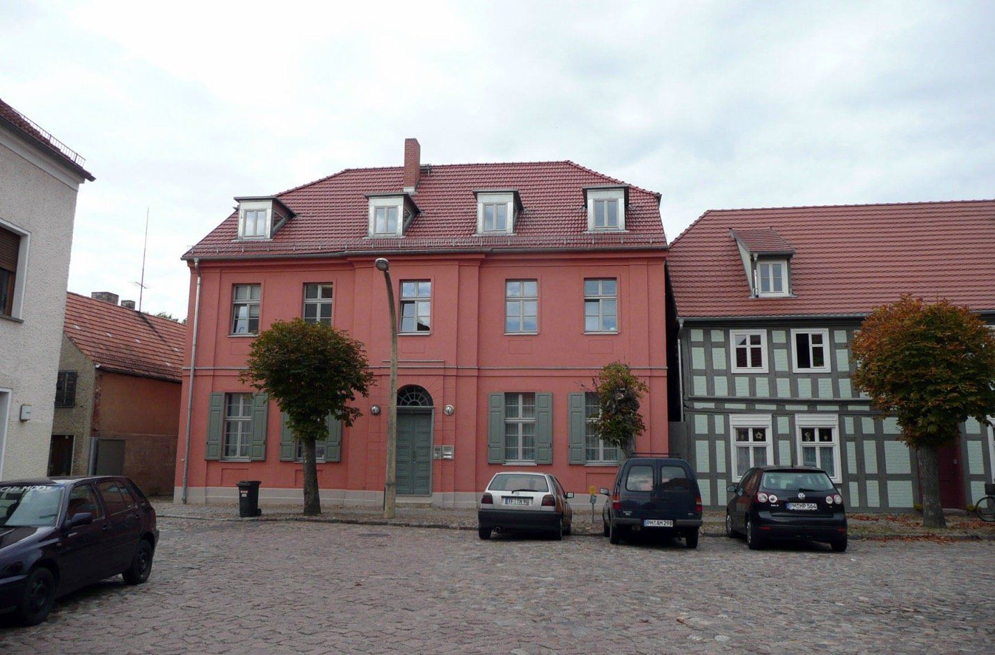 A row of cars are parked in front of a large pink building