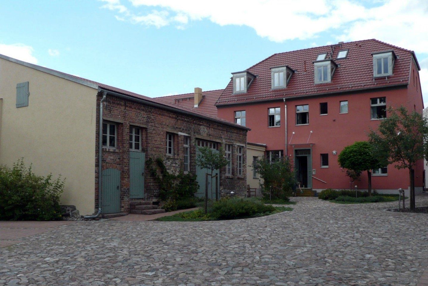 A brick building with a red roof is surrounded by a cobblestone courtyard.