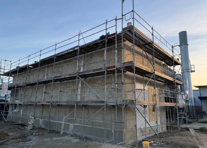Vor einem Backsteingebäude liegt ein Holzpfosten im Dreck.