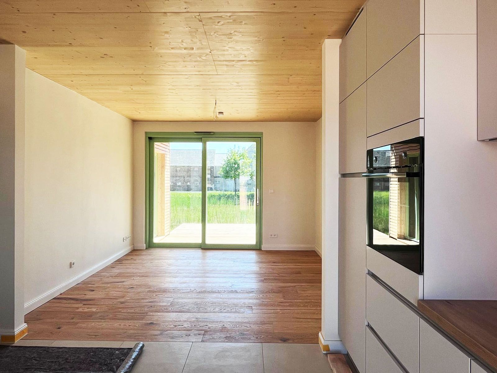 Innenansicht eines modernen Zimmers mit Holzboden und -decke, weißen Wänden und einer Glasschiebetür.