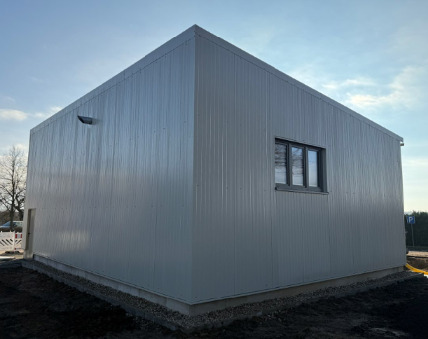 Graues Metallgebäude mit einem kleinen Fenster vor blauem Himmel.