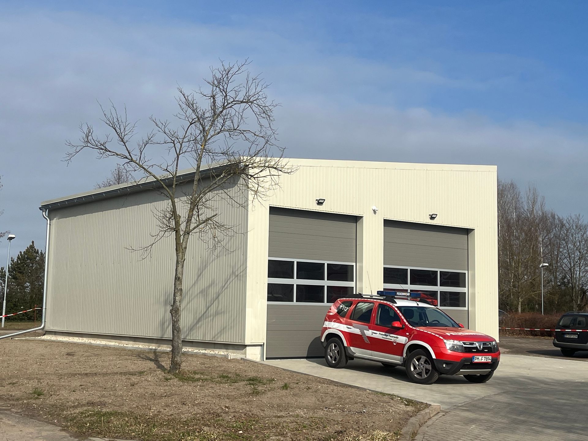 Feuerwache mit einem rot-weißen Feuerwehrauto, das vor den Garagentoren parkt.