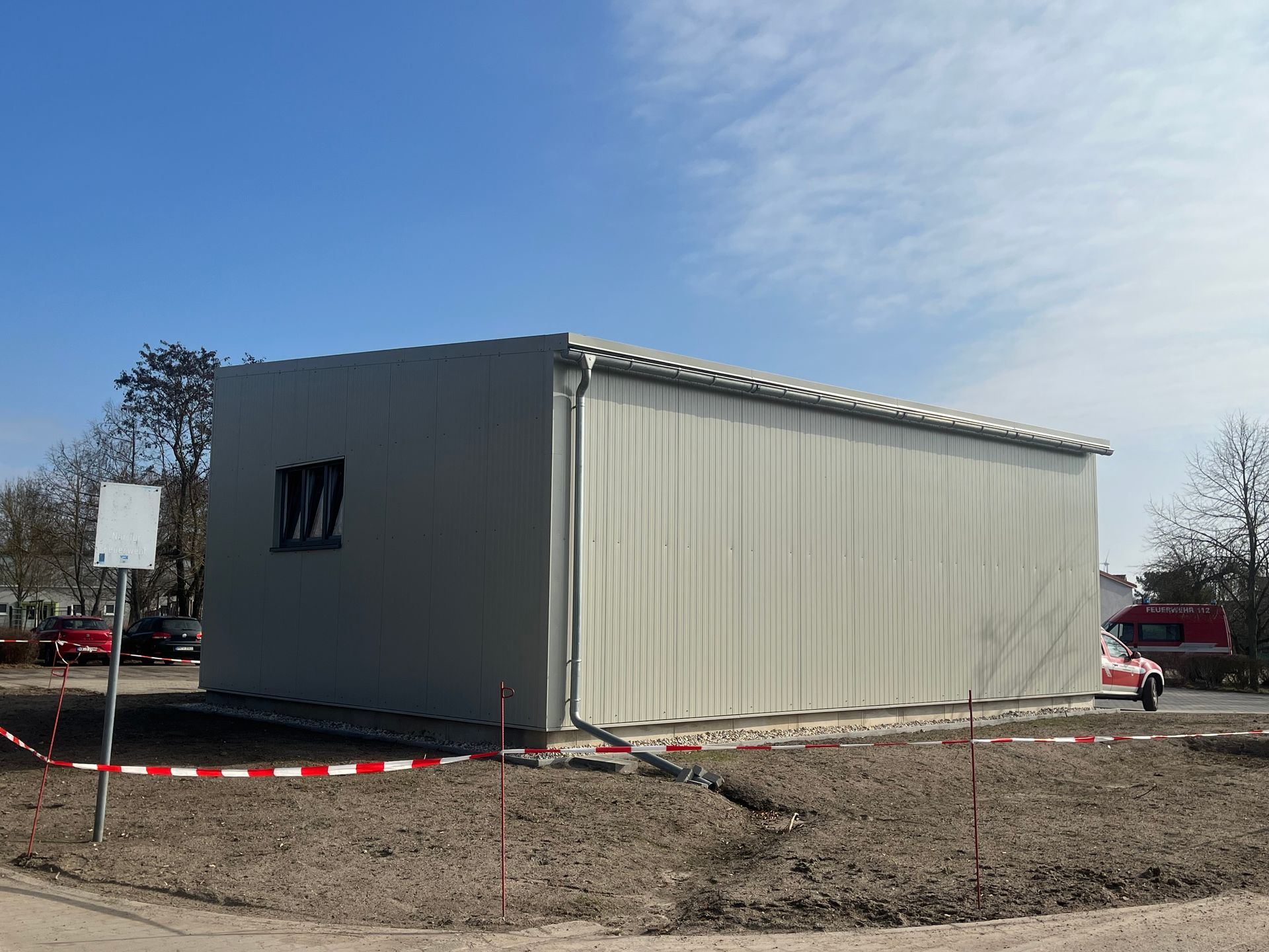 Ein helles, rechteckiges Gebäude mit einem einzigen Fenster. Außen ist es von rotem und weißem Absperrband umgeben.