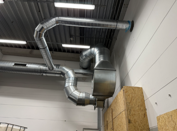 Verzinkte Metall-Lüftungskanäle und -rohre sind an einer weißen Wand angebracht.