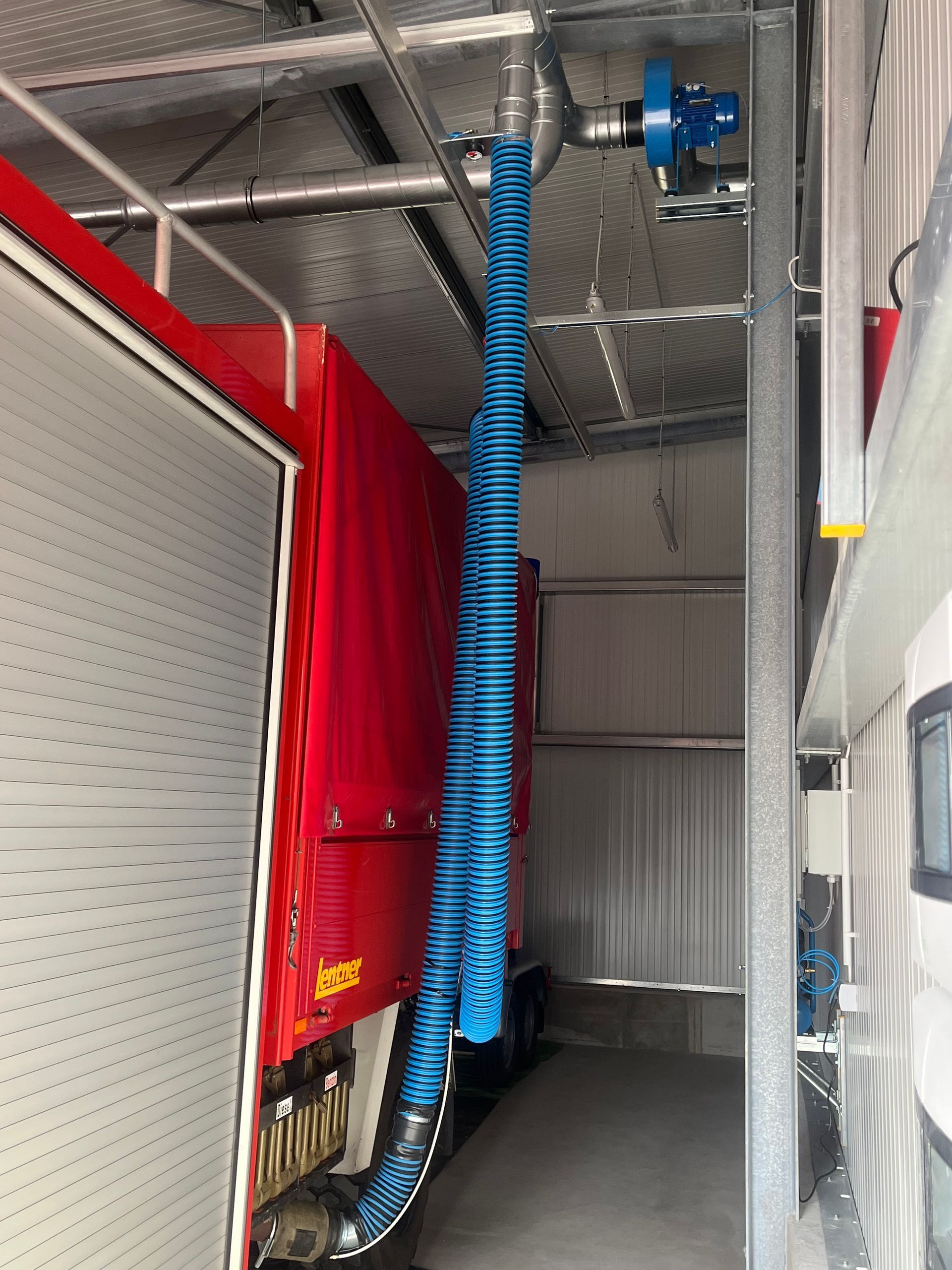 Ein blauer Schlauch hängt senkrecht in der Nähe eines roten Fahrzeugs innerhalb einer Metallkonstruktion.
