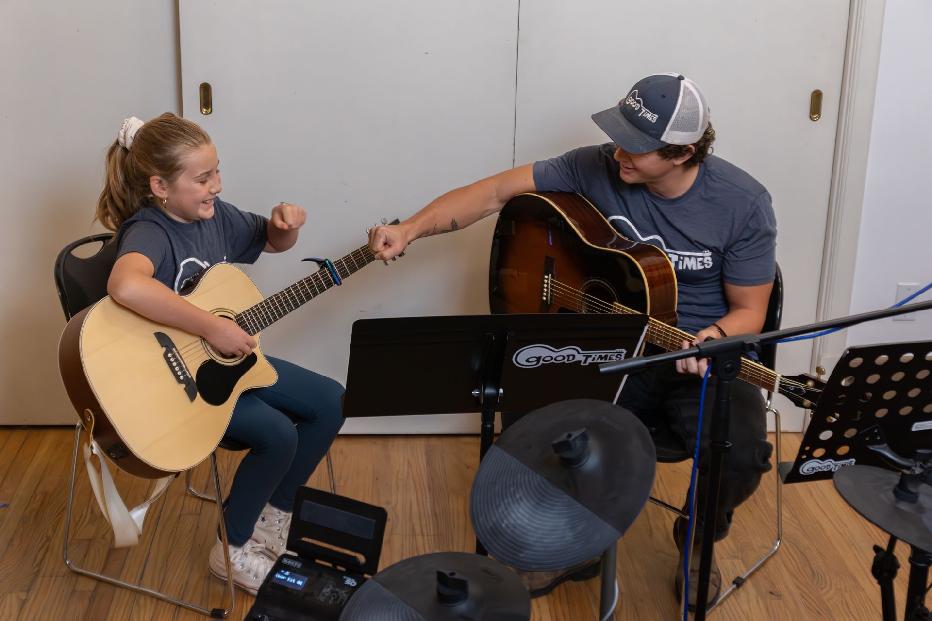 A young person and her music teacher fist bump while playing guitars in a music room.