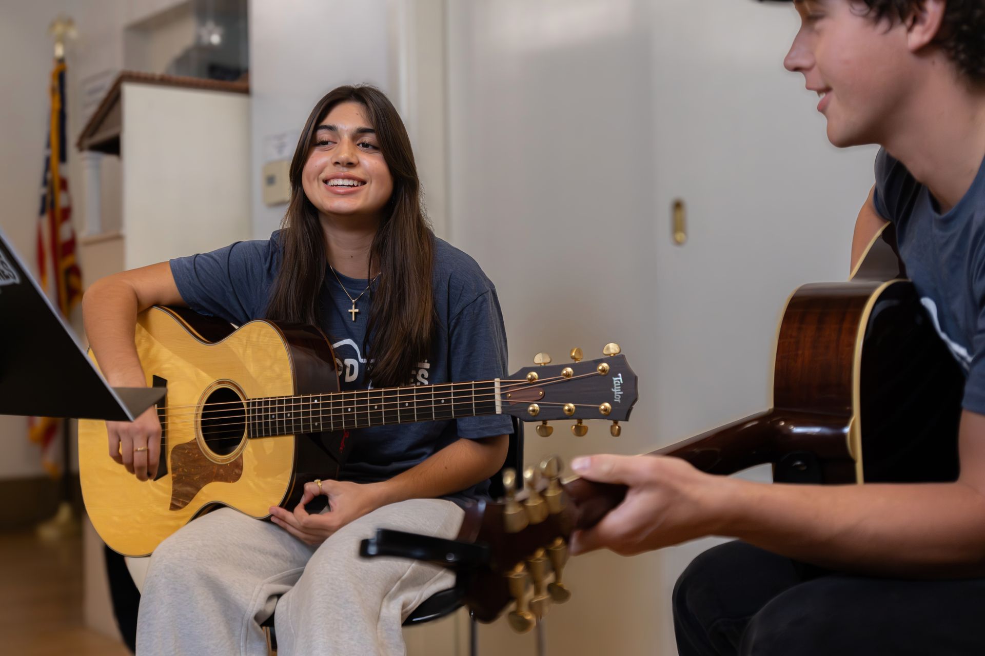 Two people with guitars, sitting and smiling; in a room.