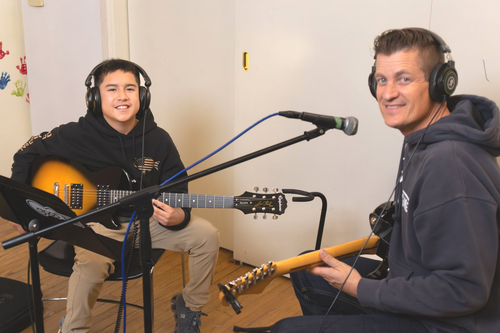 A boy and his teacher play guitar during an electric guitar music lesson.