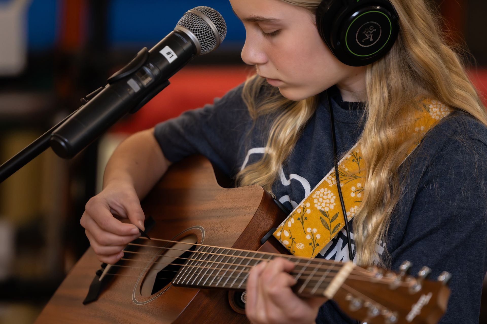 Girl playing acoustic guitar, wearing headphones and using a microphone, at band practice.